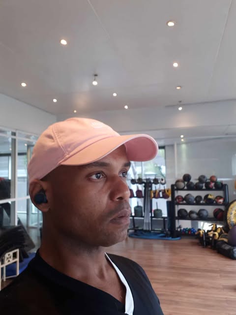 A dark-skinned man with a serious face wearing a baseball cap and earbuds.